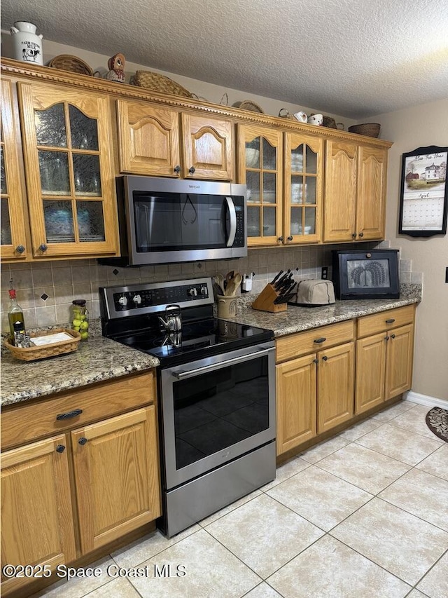 kitchen with tasteful backsplash, light tile patterned floors, appliances with stainless steel finishes, and light stone counters