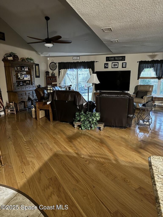 living room with ceiling fan, a textured ceiling, wood-type flooring, and a healthy amount of sunlight