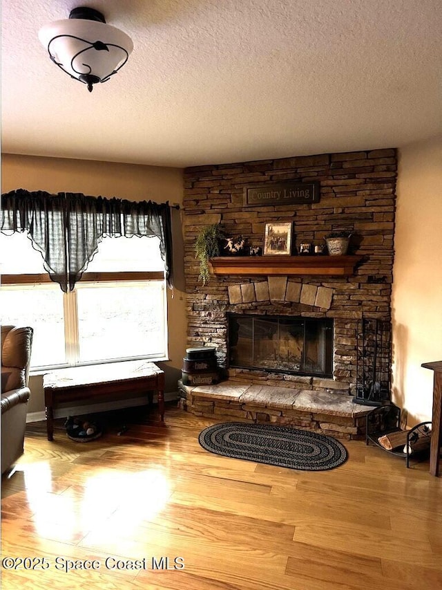 living area with hardwood / wood-style flooring, a textured ceiling, and a stone fireplace