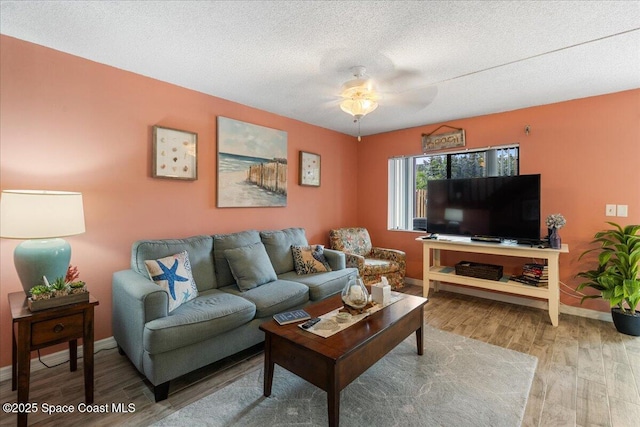 living room with ceiling fan, a textured ceiling, and light wood-type flooring