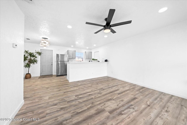 unfurnished living room featuring light wood-style floors, recessed lighting, a textured ceiling, and baseboards