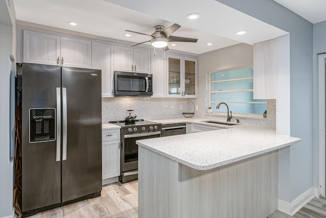 kitchen with stainless steel appliances, sink, light stone counters, light wood-type flooring, and kitchen peninsula