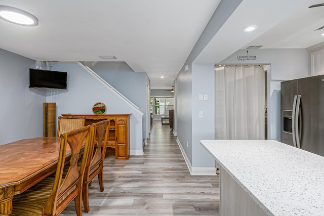 kitchen with stainless steel refrigerator with ice dispenser, light wood-type flooring, and light stone counters