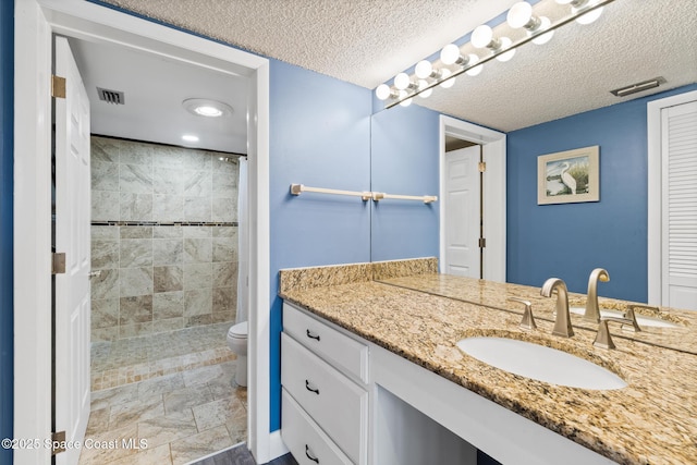 bathroom with toilet, tiled shower, a textured ceiling, and vanity