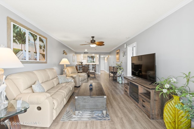 living room featuring light wood-type flooring, ceiling fan, and ornamental molding