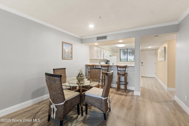 dining room with crown molding, light hardwood / wood-style flooring, and a textured ceiling