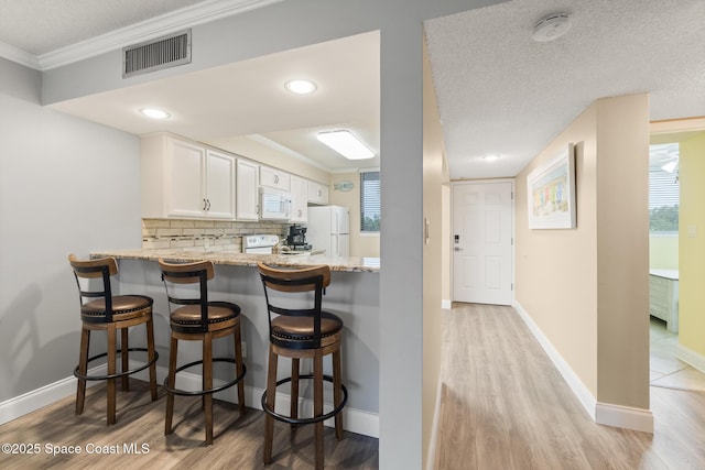 kitchen with backsplash, light wood-type flooring, white cabinets, light stone counters, and white appliances