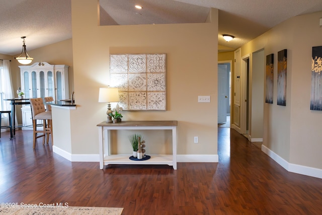 hall with dark wood-type flooring, a textured ceiling, and vaulted ceiling