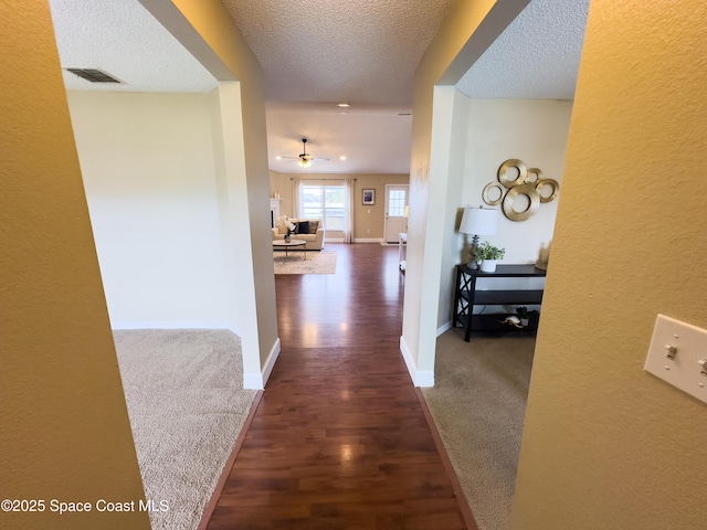 hall with dark carpet and a textured ceiling