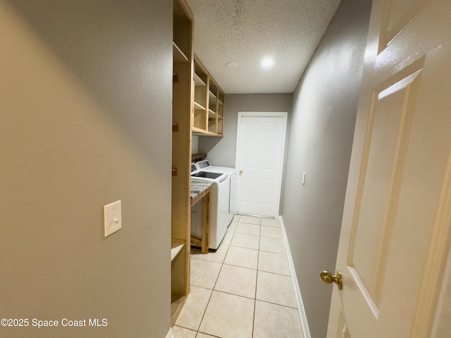 clothes washing area with washing machine and dryer, a textured ceiling, and light tile patterned floors