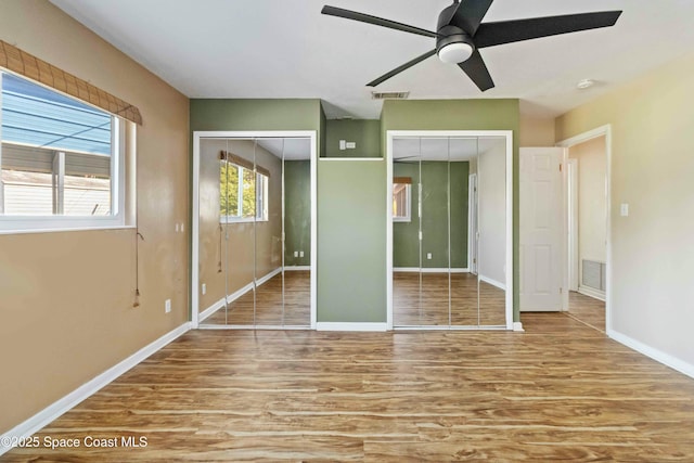 unfurnished bedroom featuring hardwood / wood-style flooring, two closets, and ceiling fan