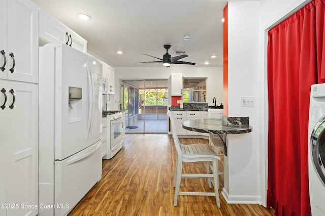 kitchen with white appliances, white cabinets, washer / clothes dryer, wood-type flooring, and dark stone countertops