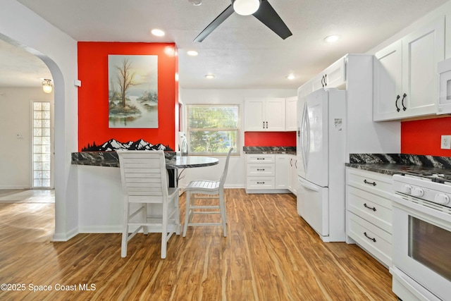 kitchen with white appliances, light hardwood / wood-style floors, white cabinetry, a breakfast bar, and ceiling fan