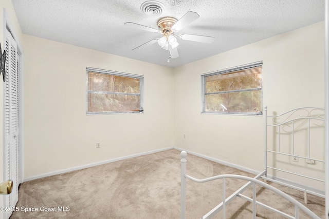 unfurnished bedroom featuring ceiling fan, a textured ceiling, a closet, and carpet floors