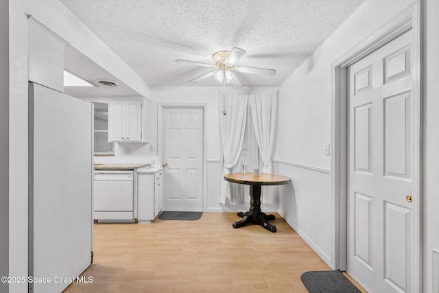 interior space with ceiling fan, refrigerator, white dishwasher, light hardwood / wood-style flooring, and white cabinets