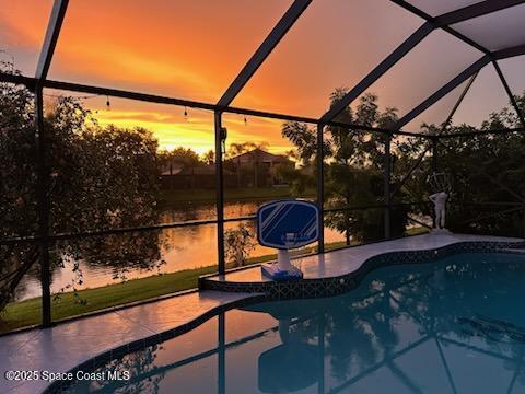 pool at dusk with a patio, a water view, and a lanai