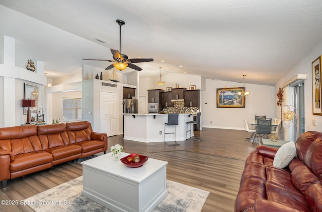 living room featuring ceiling fan with notable chandelier, a textured ceiling, dark hardwood / wood-style flooring, and vaulted ceiling