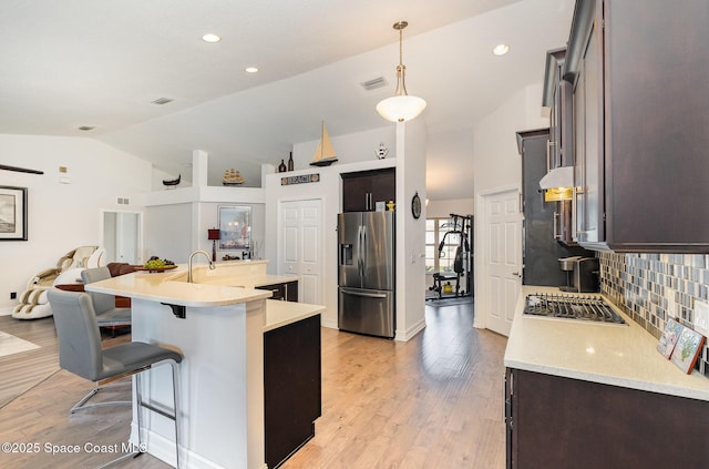 kitchen with a kitchen island with sink, a kitchen breakfast bar, backsplash, stainless steel appliances, and lofted ceiling