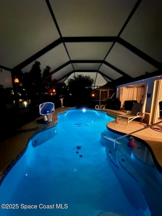 pool at night with glass enclosure and a patio