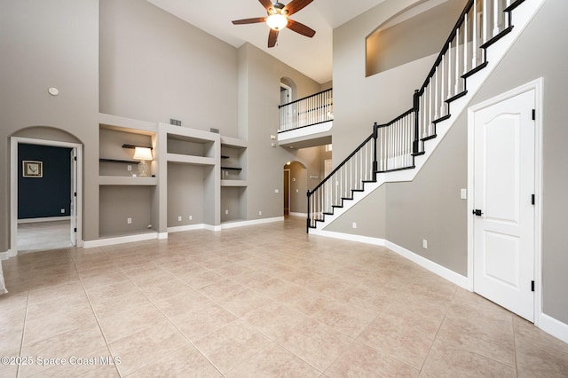 unfurnished living room featuring ceiling fan, light tile patterned floors, built in features, and a towering ceiling