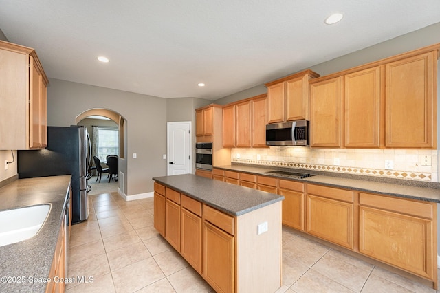 kitchen with appliances with stainless steel finishes, sink, tasteful backsplash, light tile patterned floors, and a kitchen island