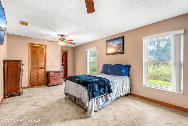 tiled bedroom with ceiling fan, a closet, and a textured ceiling