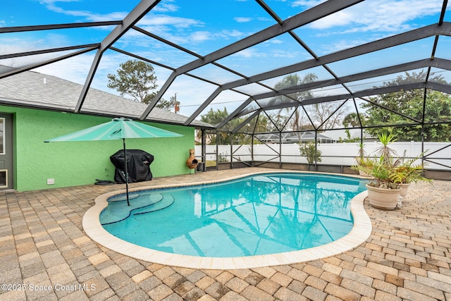 view of swimming pool with a grill, a patio area, and glass enclosure