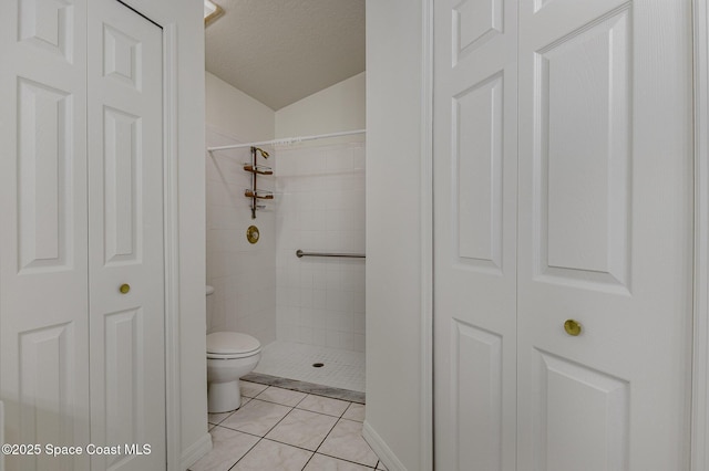 bathroom featuring a textured ceiling, tile patterned flooring, a tile shower, and toilet