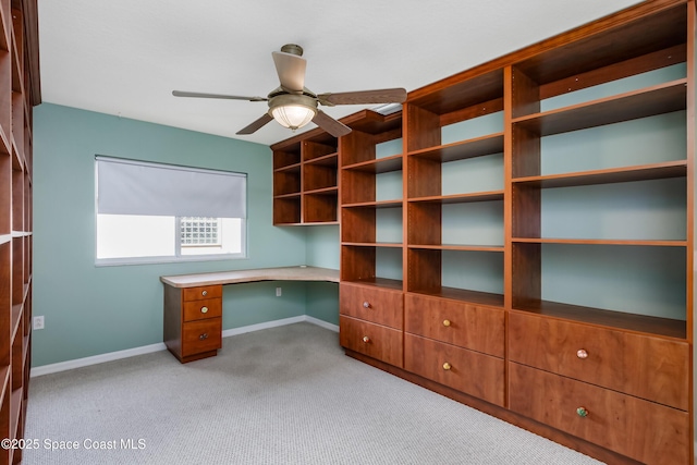 unfurnished office with built in desk, ceiling fan, and light carpet