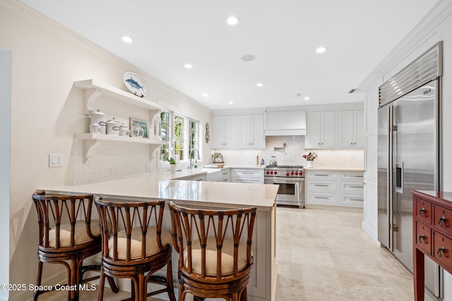 kitchen with kitchen peninsula, high end appliances, a breakfast bar, tasteful backsplash, and white cabinets