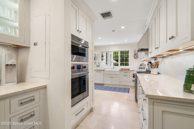 kitchen with white cabinets, backsplash, light stone counters, and range hood