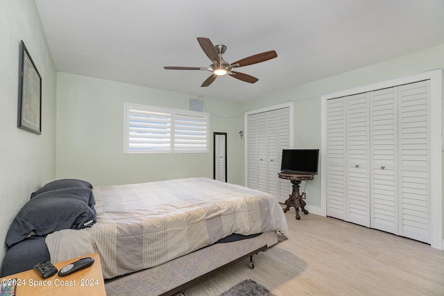 bedroom featuring ceiling fan, light hardwood / wood-style flooring, and multiple closets