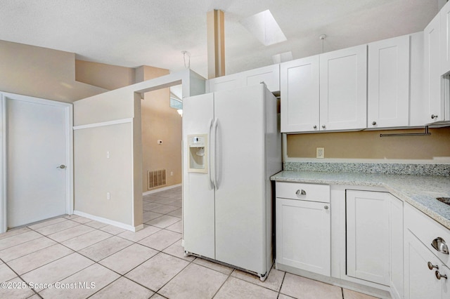 kitchen featuring white refrigerator with ice dispenser, a skylight, light tile patterned floors, light stone counters, and white cabinets