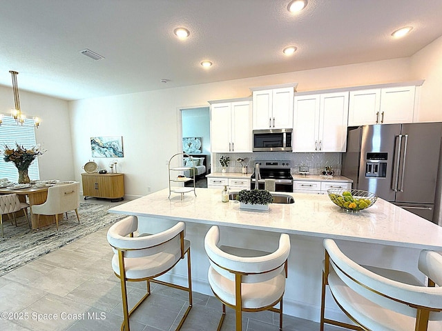 kitchen featuring white cabinets, a sink, a breakfast bar area, stainless steel appliances, and visible vents