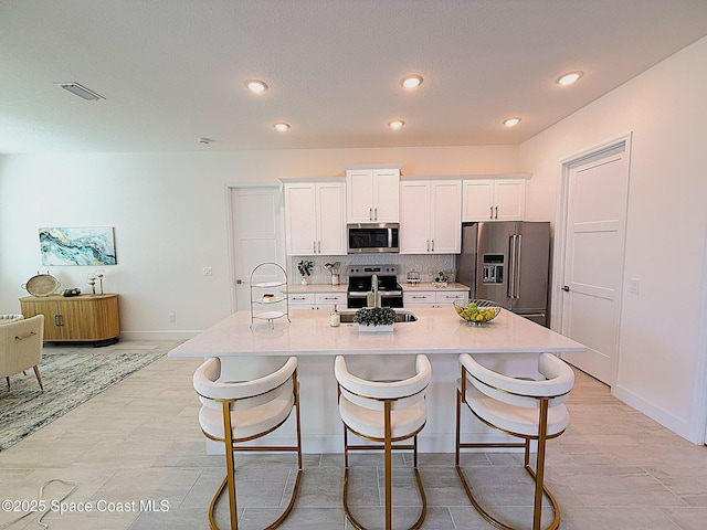 kitchen featuring visible vents, a center island with sink, white cabinetry, a sink, and stainless steel appliances