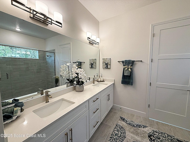 bathroom featuring double vanity, baseboards, a sink, and a stall shower