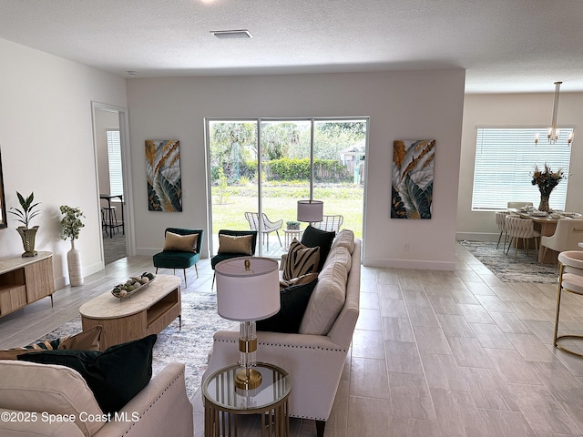 living room featuring plenty of natural light, a textured ceiling, baseboards, and a chandelier