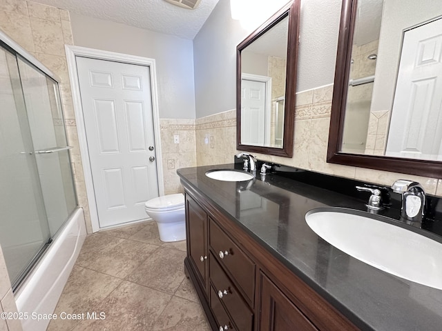 full bathroom with toilet, a textured ceiling, tile walls, and a sink