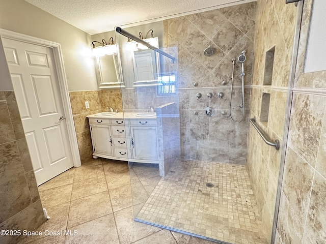 full bathroom with a sink, a textured ceiling, a tile shower, tile walls, and double vanity