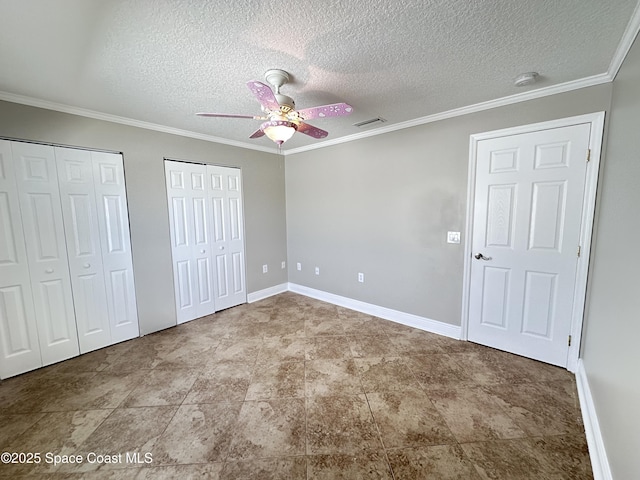 unfurnished bedroom with baseboards, visible vents, ornamental molding, a textured ceiling, and two closets