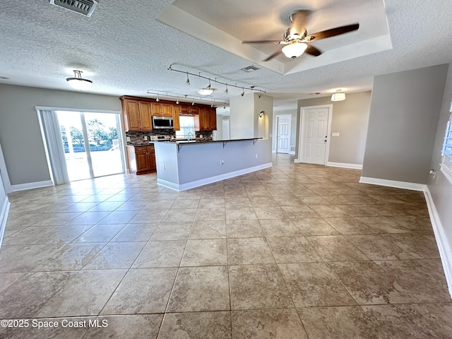 kitchen featuring visible vents, stainless steel microwave, dark countertops, open floor plan, and decorative backsplash