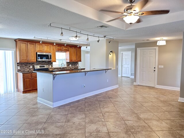 kitchen featuring visible vents, a breakfast bar, backsplash, stainless steel appliances, and brown cabinetry