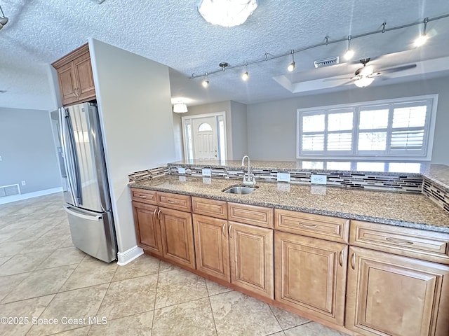 kitchen featuring a textured ceiling, light stone countertops, freestanding refrigerator, and a sink