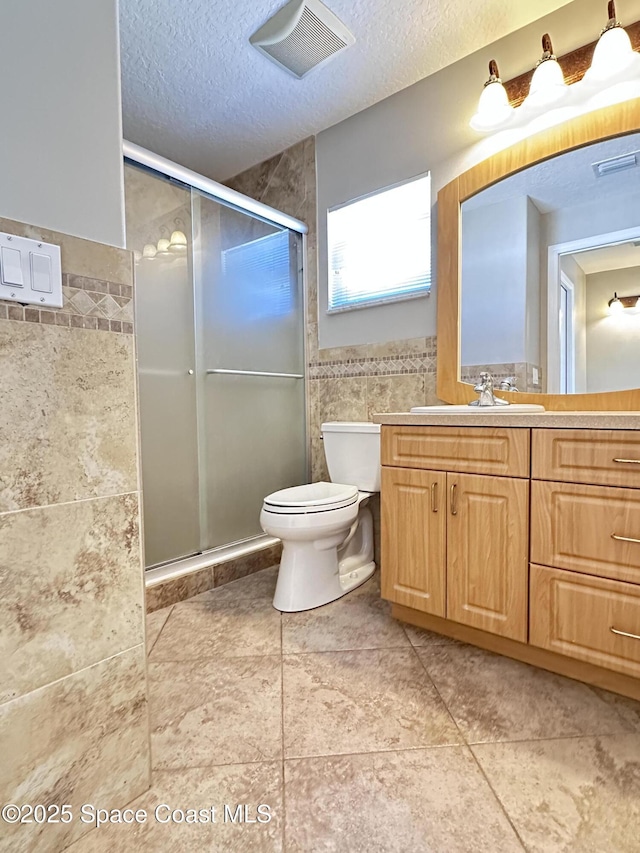 full bath with visible vents, a shower stall, tile walls, toilet, and a textured ceiling