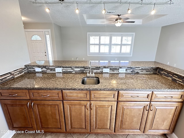 kitchen with visible vents, a tray ceiling, dark stone counters, a sink, and a textured ceiling