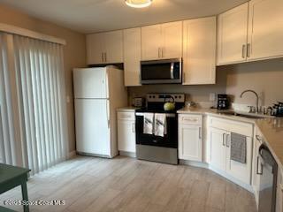 kitchen with sink, stainless steel appliances, light wood-type flooring, and white cabinetry