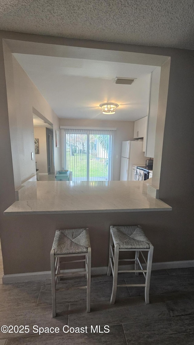 kitchen featuring a textured ceiling, kitchen peninsula, white cabinets, and white fridge