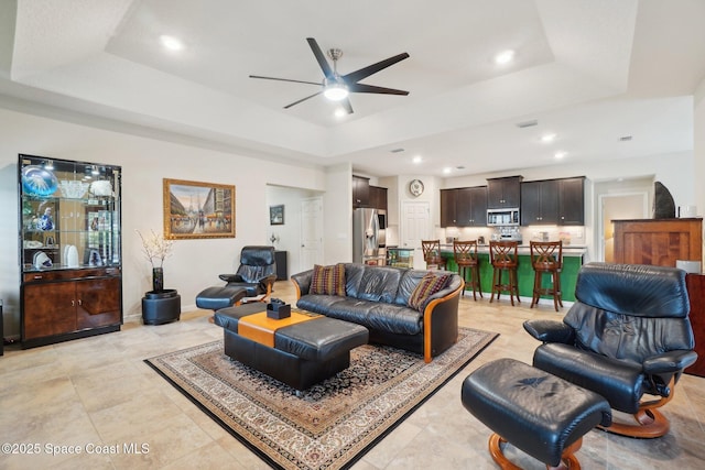 living room featuring a raised ceiling, light tile patterned floors, and ceiling fan