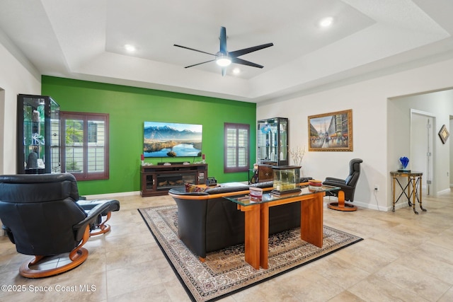 living room featuring a raised ceiling, light tile patterned floors, and ceiling fan