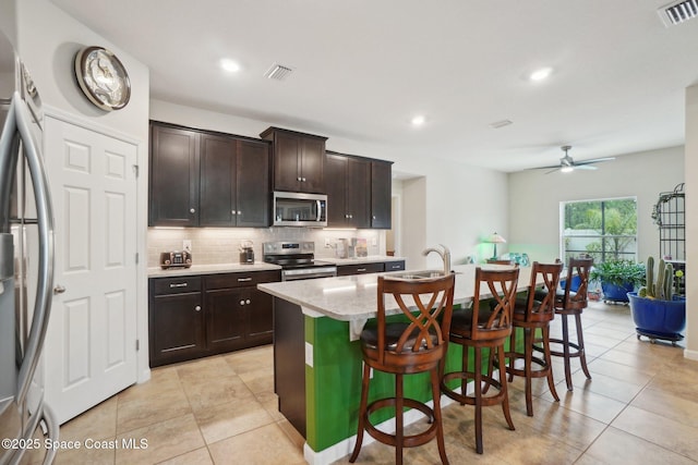 kitchen with appliances with stainless steel finishes, an island with sink, sink, a kitchen bar, and decorative backsplash